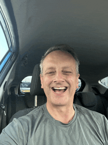 a man in a grey shirt is smiling in the back seat of a car with a license plate that starts with l on it