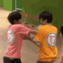 two young men are fighting each other in a room . one of the men is wearing an orange shirt with the letter t on it .