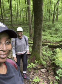 two women are hiking in the woods and one is wearing a black adidas hat