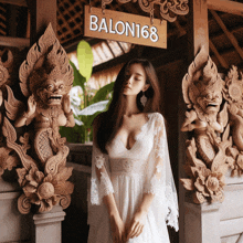 a woman in a white dress stands in front of a sign for balon168