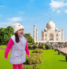 a little girl wearing a white vest and a white hat stands in front of the taj mahal