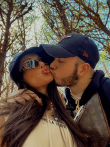 a man kisses a woman on the cheek while wearing a new era hat