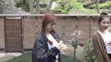 two girls are standing in front of a wooden fence and one of them is holding a bottle of water