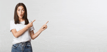 a woman in a white t-shirt and blue jeans is pointing to the right