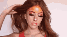 a woman with red hair and freckles is wearing a red top and has a fire face painted on her face .