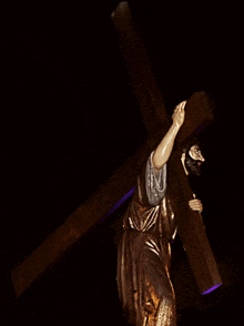 a statue of jesus carrying a wooden cross in a dark room