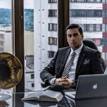 a man in a suit and tie is sitting at a desk in front of a laptop .