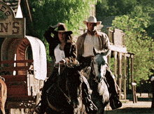 a man and a woman are riding horses in front of a sign that says ' n's ' on it