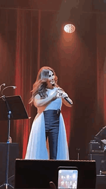 a woman in a white dress singing into a microphone on a stage