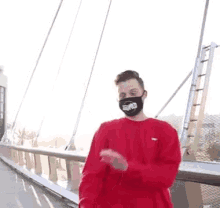 a man wearing a red sweater and a mask is standing on a bridge .