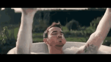 a man is laying in a bathtub with his arms outstretched and his eyes closed .