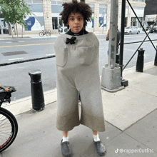 a person wearing a jumpsuit and crocs stands on a sidewalk next to a pole