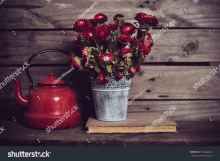 a vase of red flowers sits next to a red tea kettle