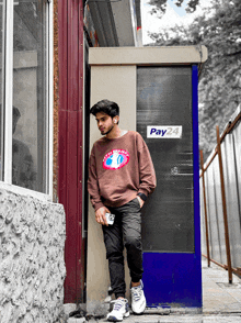 a man leaning against a wall with a pay24 sign on it