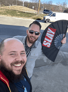 two men are posing for a picture and one has a fan that says slay on it