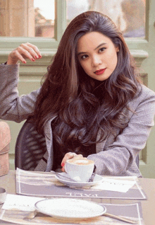 a woman is sitting at a table with a cup of coffee and a plate with the word tivoli on it