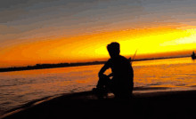 a man sits on the shore of a lake at sunset holding a fishing rod