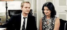 a man in a suit and tie is sitting next to a woman in a leopard print dress in an office .