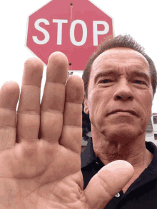 arnold schwarzenegger shows his hand in front of a stop sign