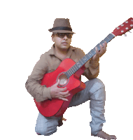 a man in a hat is kneeling down holding a red guitar