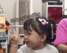 a little girl with a rainbow hair clip is making a funny face with the words chày nuoc mieng above her head