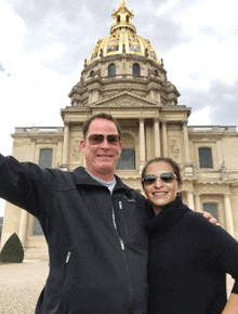 a man and a woman posing in front of a large building