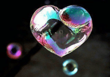 a heart shaped soap bubble is floating in the air with other soap bubbles .