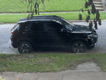 a black suv is parked on a sidewalk next to a tree