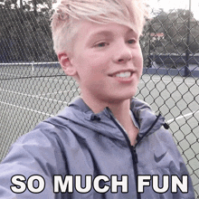 a young boy is smiling in front of a chain link fence with the words so much fun written on it