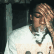 a man with a tattoo on his arm is smoking a cigarette and drinking from a glass .