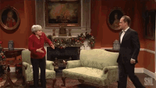 a man and woman are standing in a living room with snl written on the bottom right