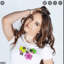 a woman is holding her hair in a bun while wearing a white t-shirt with letters on it .