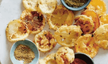 a white plate topped with fried lemon slices and bowls of sauces