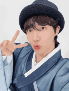 a young man wearing a black hat and a blue kimono is making a peace sign