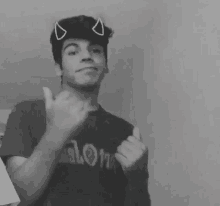 a black and white photo of a young man with devil horns on his head giving a thumbs up .