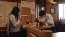 a man and a woman sit at a table in a restaurant with a menu on the wall above them