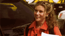 a woman in an orange coat is smiling in front of a car that says ' ford ' on the windshield