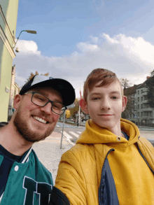 a man and a boy are posing for a picture and the boy is wearing a yellow jacket with the letter h on it