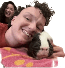 a man with curly hair is laying on a pink towel with a black and white guinea pig