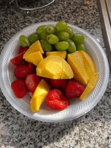 a paper plate filled with fruit including strawberries mangoes and grapes