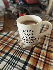 a mug that says love you to the moon and back sits on a plaid table cloth