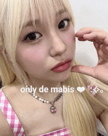 a girl with blonde hair is wearing a pink plaid top and a necklace with a pink pendant