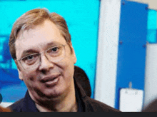 a man wearing glasses is smiling in front of a blue background