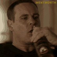 a man is drinking from a bottle with the word wentworth behind him