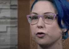 a woman with blue hair wearing glasses and face shaped earrings