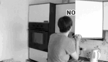 a black and white photo of a man in a kitchen with a sign that says `` no '' .