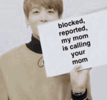 a person is holding a sign that says blocked reported my mom is calling your mom .