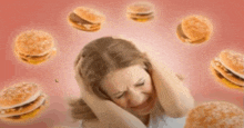 a woman is covering her ears while hamburgers are flying around her head