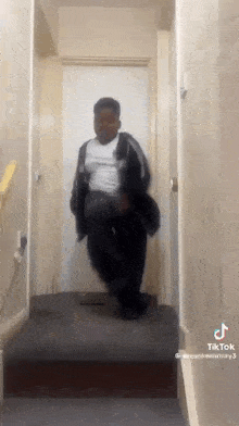 a young man is dancing in a hallway while wearing a black jacket .