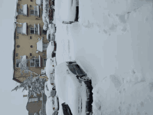 a row of cars are covered in snow in front of a brick building